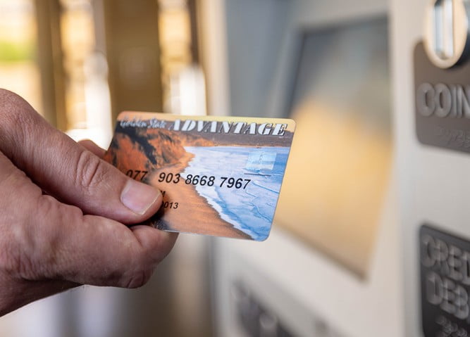 A hand holding a golden state advantage card in front of a ticket machine